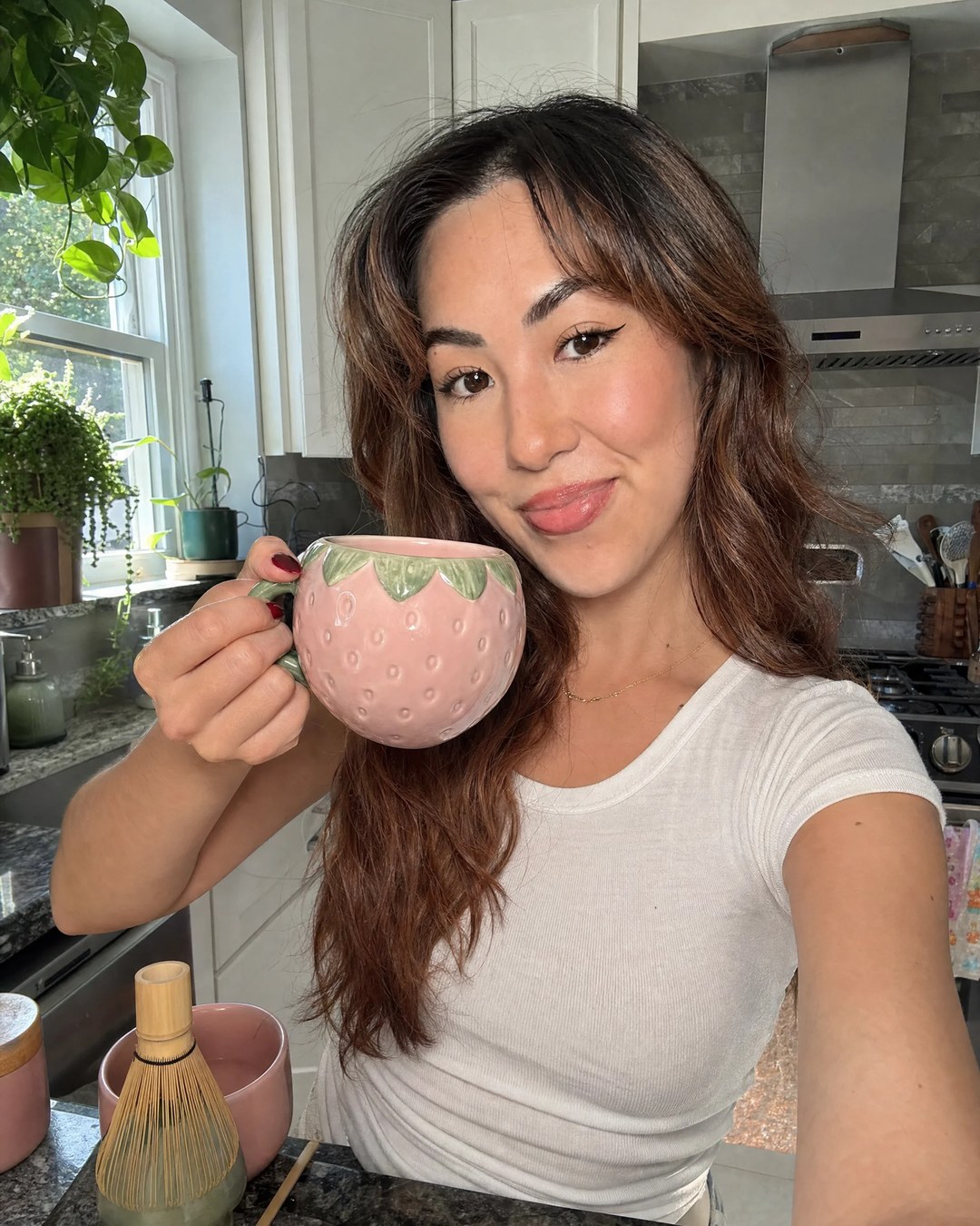 Gracey in her kitchen holding a strawberry-shaped mug next to her matcha whisk